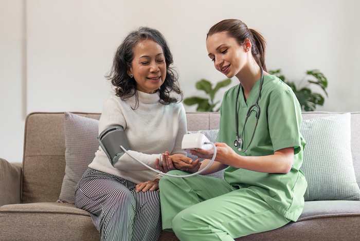 Pflegerin misst Blutdruck bei älterer Dame - Behandlungspflege