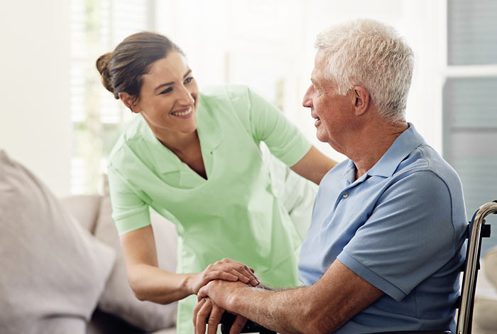 Pflegerin redet mit älterem Mann im Rollstuhl - Kurzzeitpflege
